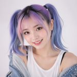 Jovem mulher sorridente com cabelo colorido e aparência inspirada em anime, em um estúdio com fundo neutro e iluminação suave.