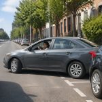 Motorista dirigindo um carro para estacionar paralelamente entre dois veículos em uma rua da cidade.