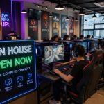 Interior de uma lan house moderna com pessoas jogando em computadores, ambiente bem iluminado e organizado.